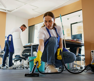 Professional cleaners from The Clean Collective working in an office – one technician using a steam cleaner on the floor while another tidies the space in the background.