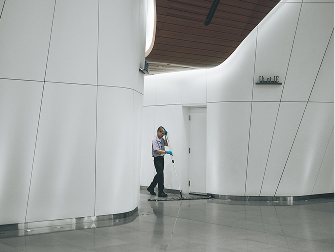 Commercial cleaner mopping the floor in a modern, white office building corridor.